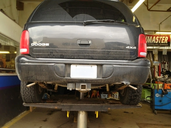 Rear view of a black GMC Yukon SUV raised on a shop lift for catalytic converter repair