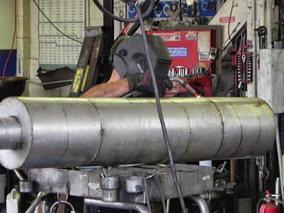 Close-up of a technician welding a large custom exhaust pipe section