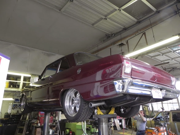 Maroon vintage classic sedan raised high on a post lift inside the auto garage