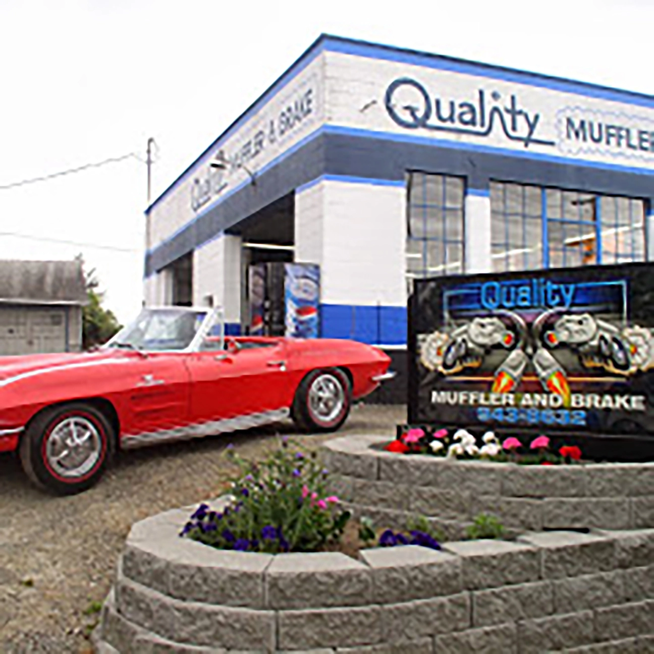 Red vintage convertible classic car parked in front of Quality Muffler and Brake sign