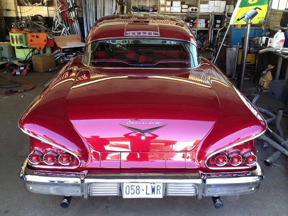 Rear view of a classic red 1958 Chevrolet car inside the garage workshop