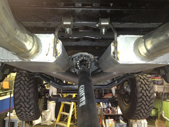 Underside view of truck chassis showing drive shaft and dual mufflers