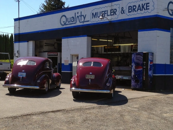 Two vintage dark red cars parked outside the service bays of Quality Muffler and Brake