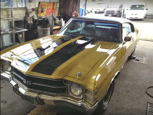 Yellow vintage Chevrolet Impala muscle car with black racing stripes inside auto shop.webp